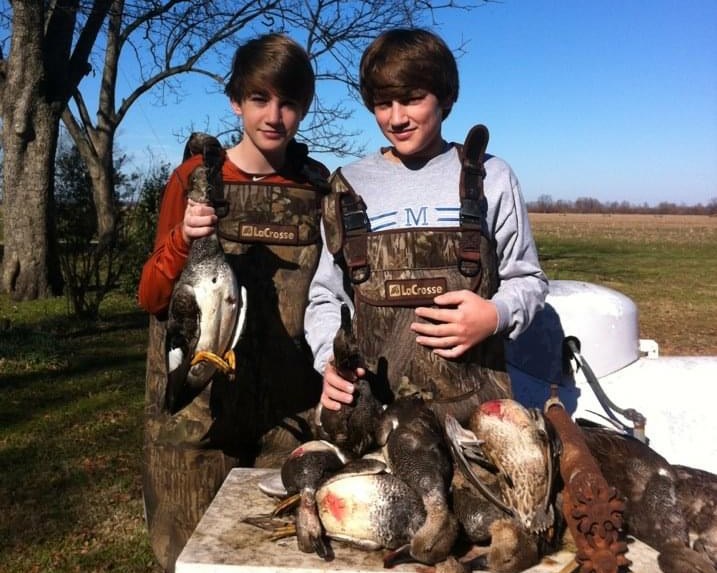 Logan and Preston in waders, holding up the morning's mallards and gadwalls